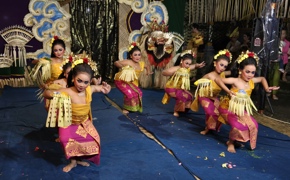 Balinese girls in ornate costumes perform a synchronized traditional dance on stage, rich in colour, energy, and cultural flair. 