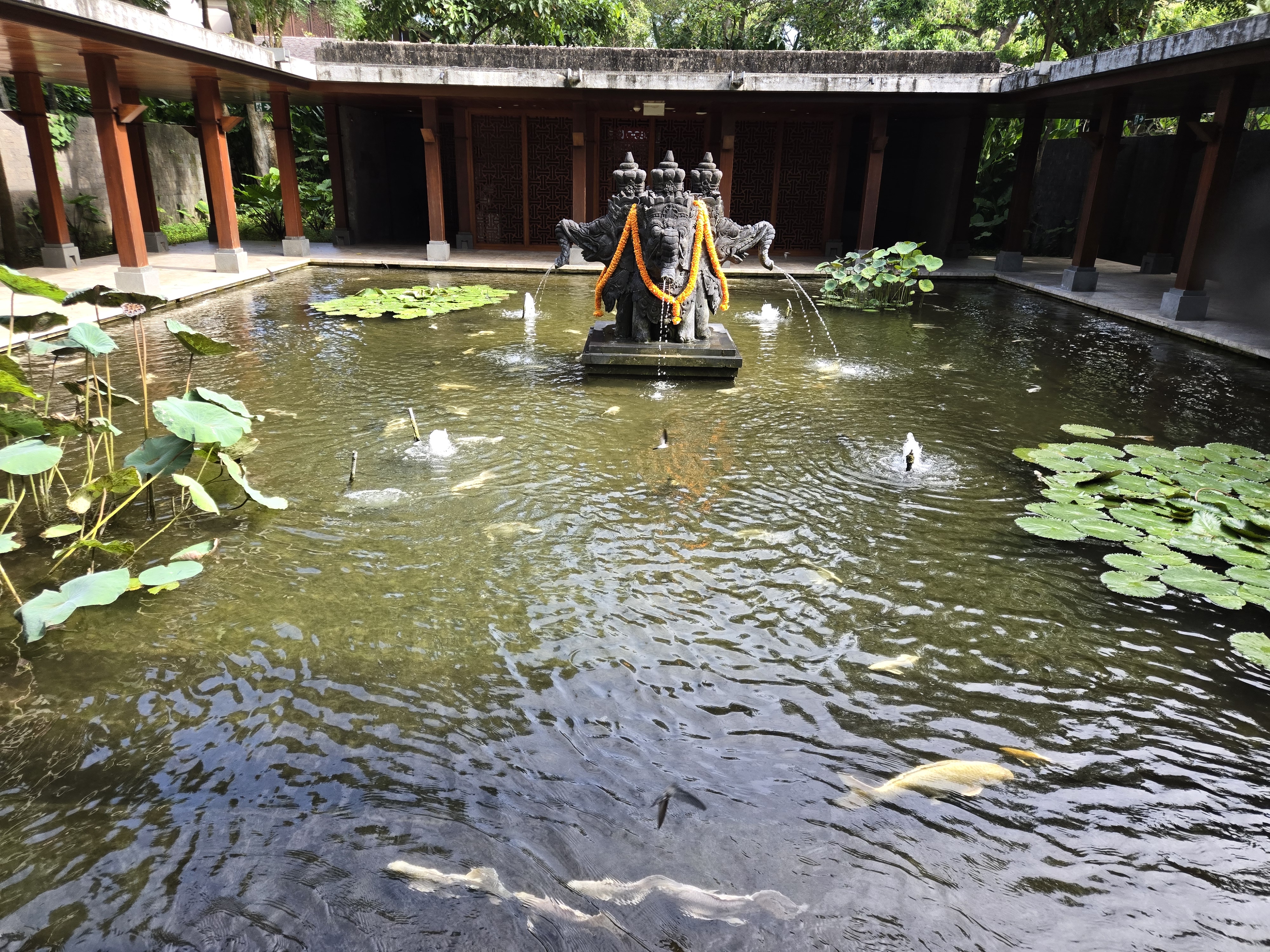 A sacred statue draped in cloth rises from a lotus pond in a peaceful courtyard in Bali, Indonesia. 