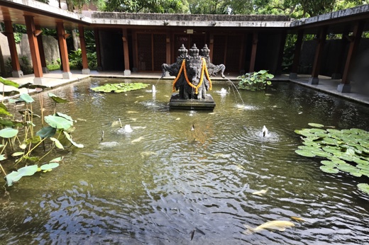 A sacred statue draped in cloth rises from a lotus pond in a peaceful courtyard in Bali, Indonesia. 