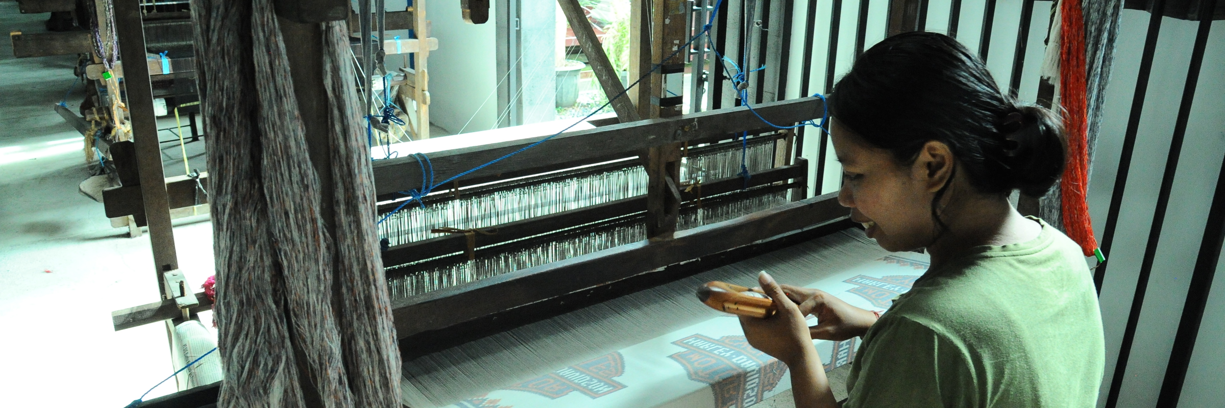 Indonesian woman weaving fabric on a traditional wooden loom in a textile workshop using natural yarns. 