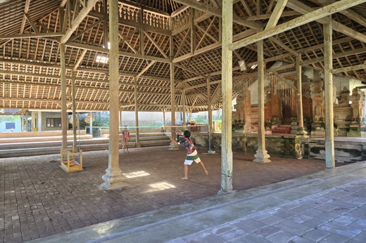 Children playing badminton inside a traditional wooden pavilion with high thatched roof in Bali, Indonesia. 