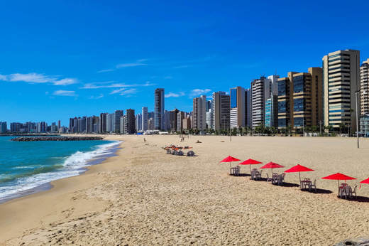 Wide sandy beach in Fortaleza with red umbrellas and a modern skyline along the northeastern coast of Brazil. 