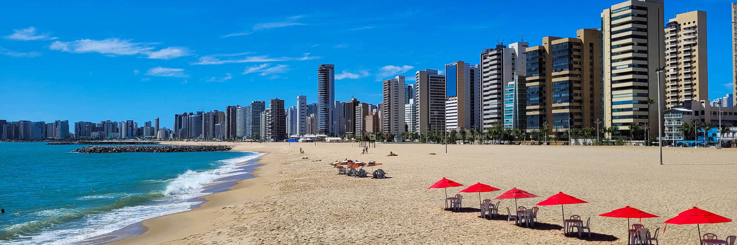 Wide sandy beach in Fortaleza with red umbrellas and a modern skyline along the northeastern coast of Brazil. 