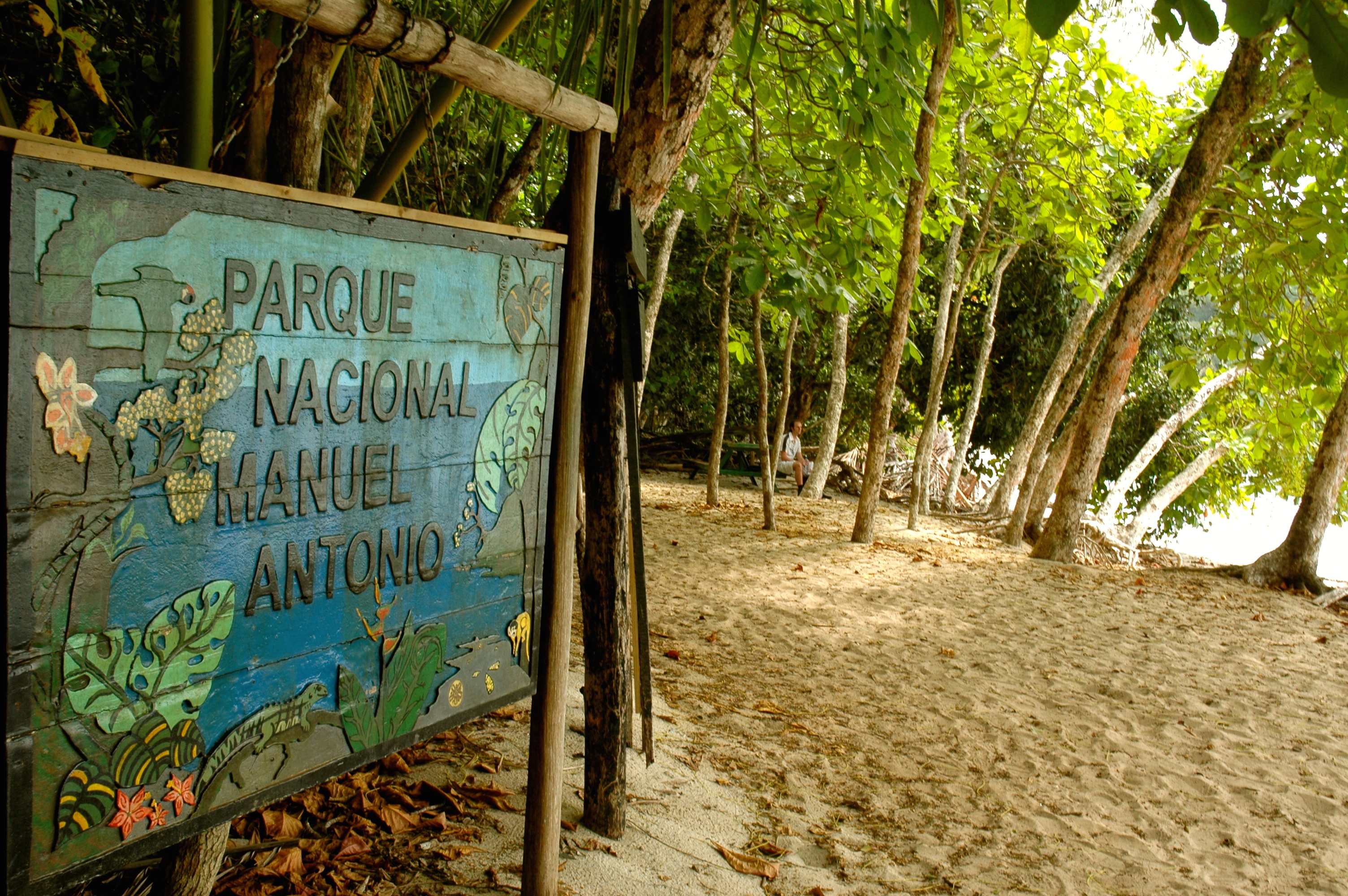 Wooden sign for Parque Nacional Manuel Antonio set beside a forested path leading to the beach. 