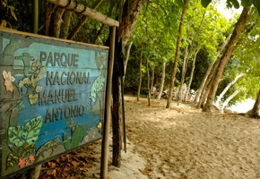 Wooden sign for Parque Nacional Manuel Antonio set beside a forested path leading to the beach. 