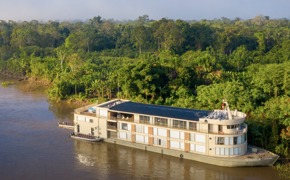 Aerial view of the Delfin III luxury river cruise gliding through the lush green Amazon rainforest in Peru. 